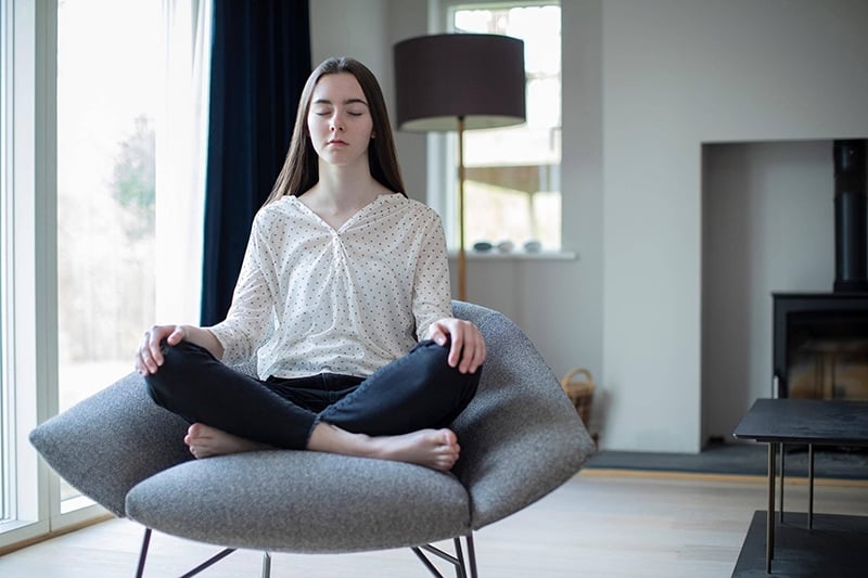 Young woman sits crossed leg in a chair while meditating