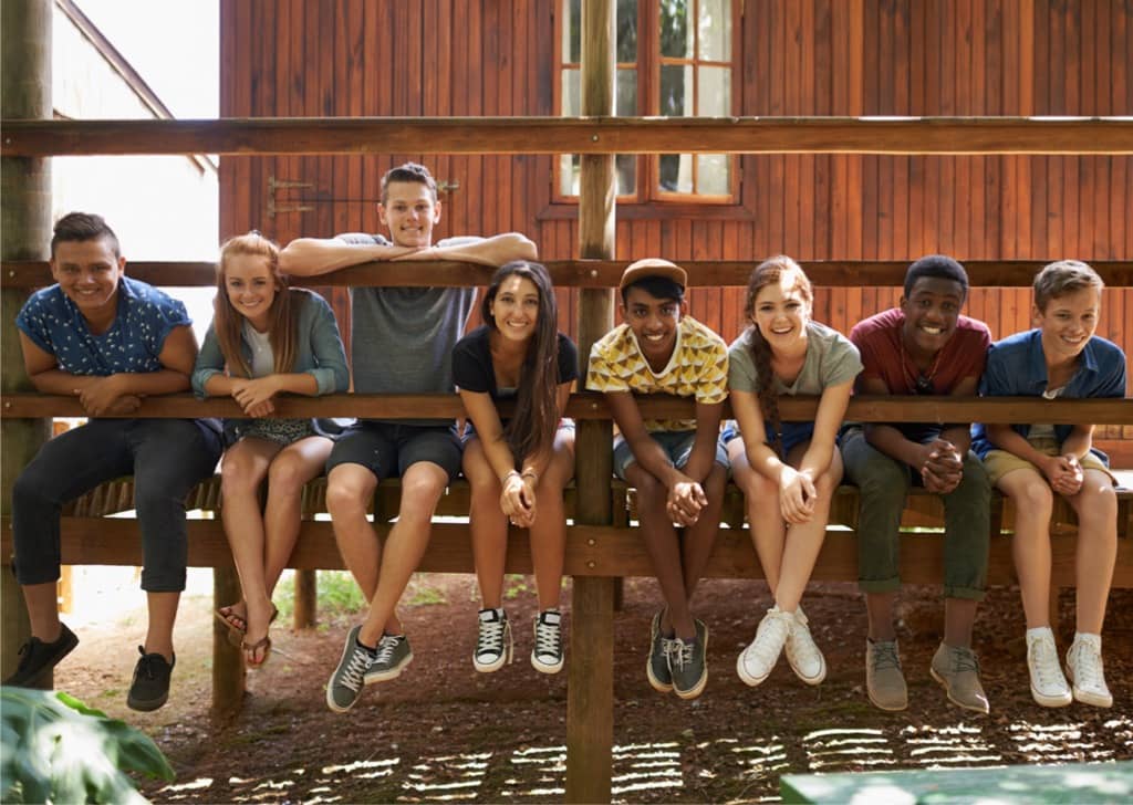 Row of smiling teens sitting on the deck of a cabin