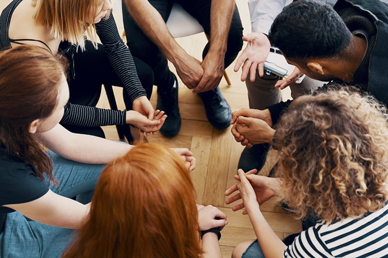 Group of young adults sitting in a circle looking towards the ground