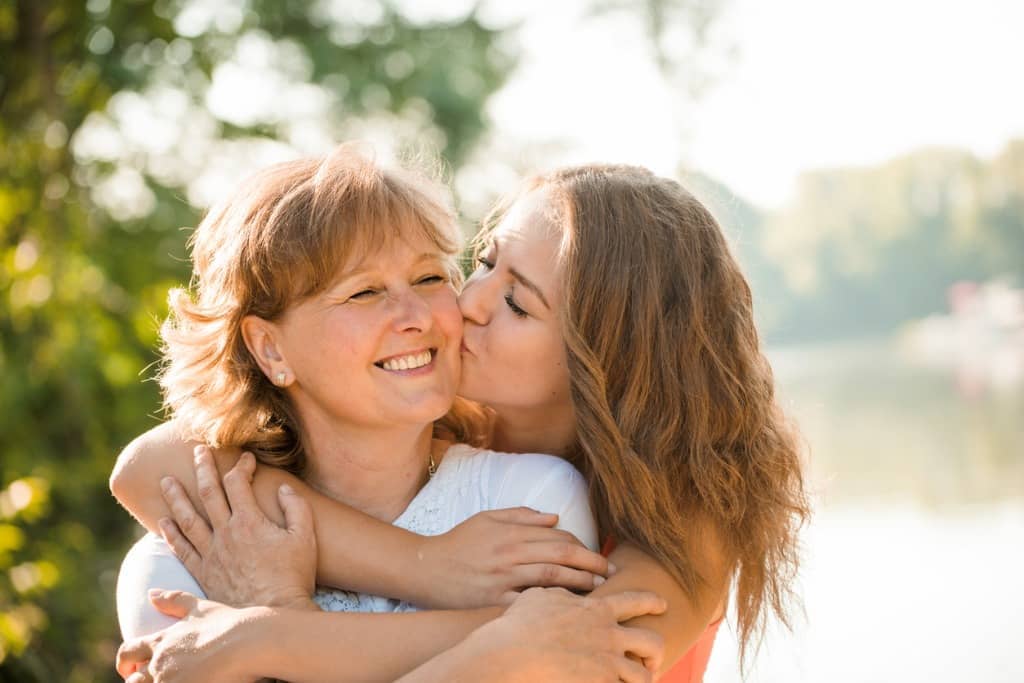 Teen daughter hugs her mom from behind