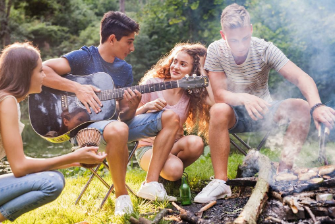 Kid playing guitar around a camp fire with other kids