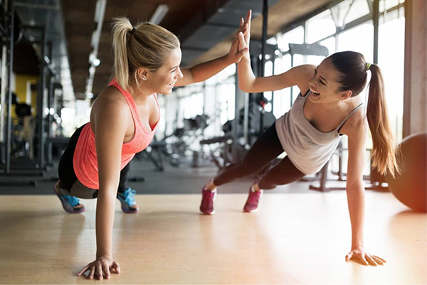 Two young women high five while doing pushups in a gym