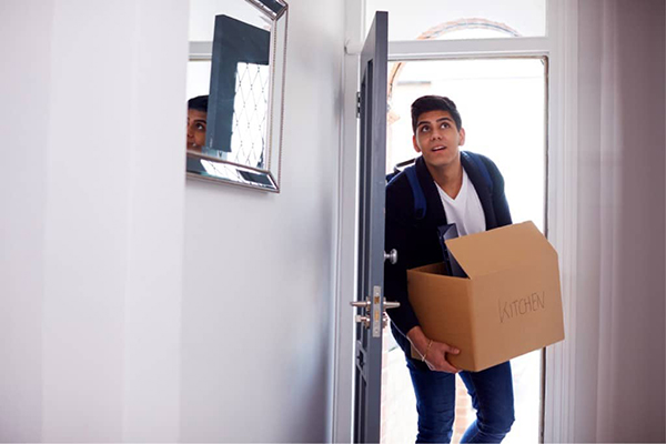 Young adult male carries a box through his front door