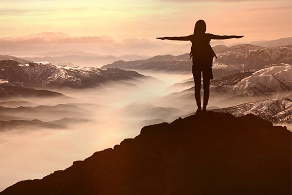 Young adult hiker stands on top of a mountain with arms outstretched